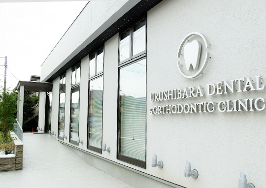 鴻巣市の漆原歯科・矯正歯科クリニックの外観。白を基調としたモダンな建物と医院ロゴの看板