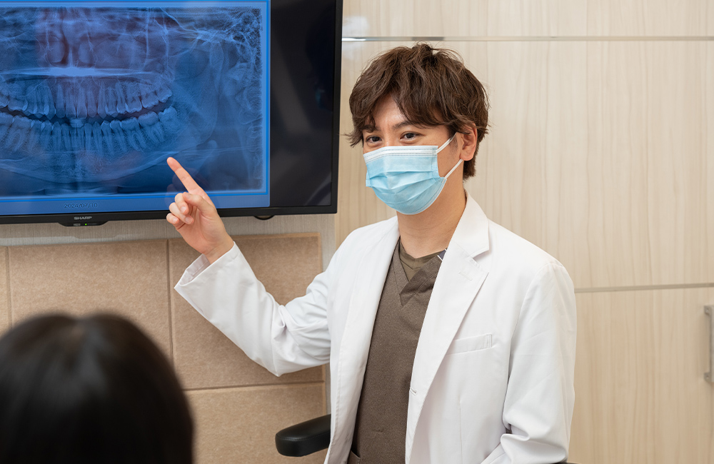 漆原歯科・矯正歯科クリニックの院長。レントゲン画像で治療方針を丁寧に説明する、安心感のある対話風景